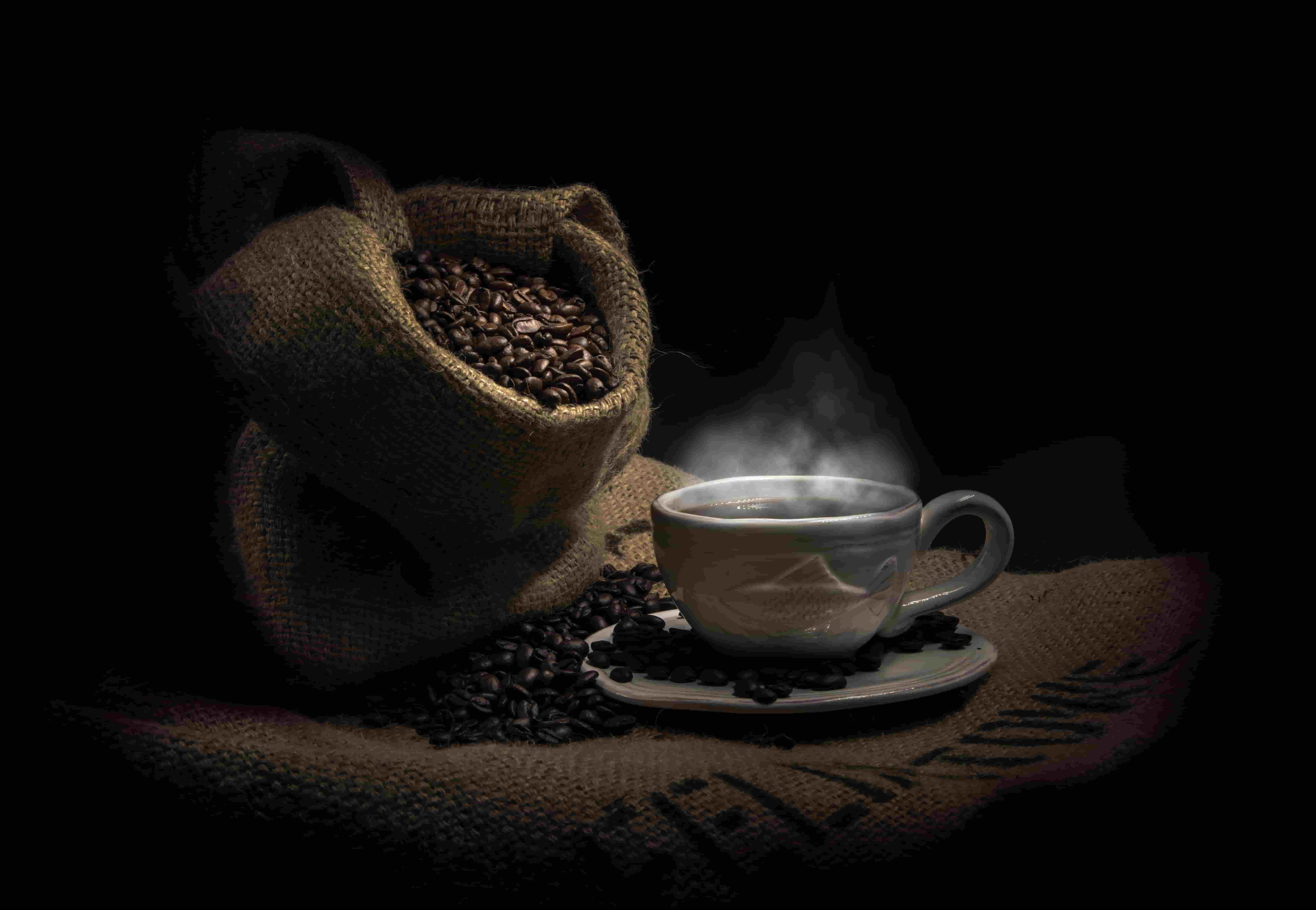 Una taza de café caliente con una bolsa de granos de café al lado.